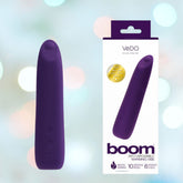 A purple VeDO Boom Rechargeable Warming Bullet Vibrator is displayed next to its packaging. The box showcases the "VeDO" brand and emphasizes features such as "10 Vibration Modes," "6 Intensity Levels," and "Waterproof Submersible," all set against a blurred background with soft light spots, promising pulsating pleasure.